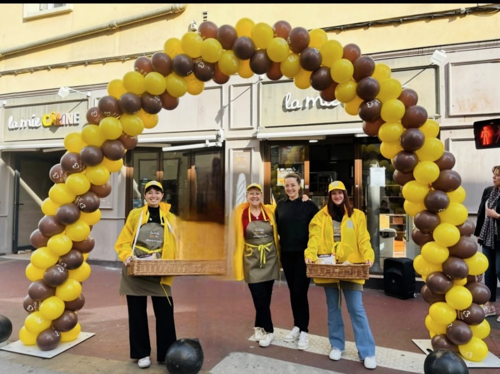 Équipe La Mie Câline devant la boutique, sous une arche de ballons jaunes et marron, lors d’une animation.